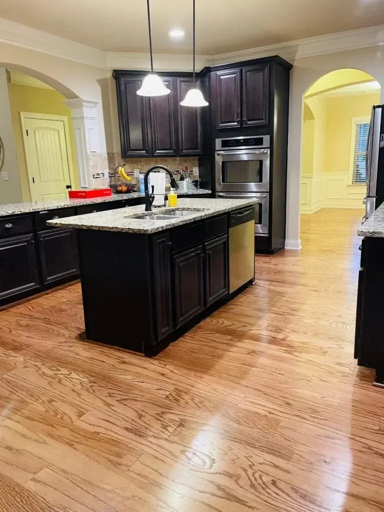 Warm-toned hardwood floor beside a dark kitchen island, a Bulldog Flooring job